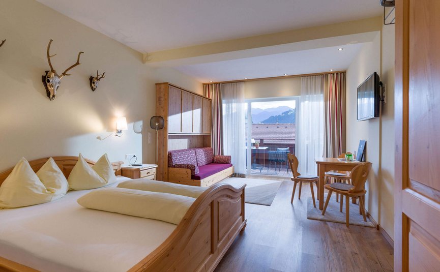 Hell eingerichtetes Hotelzimmer mit Holzmöbeln und Bergblick vom Balkon