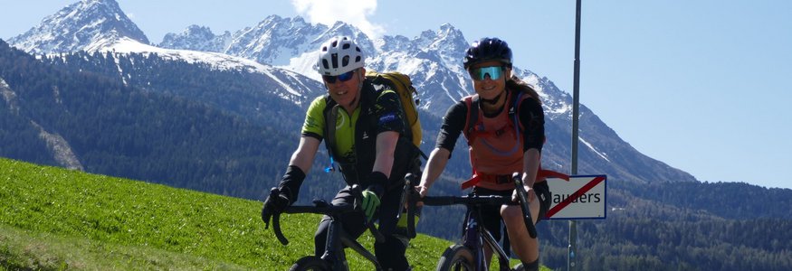 Zwei Radfahrer fahren auf Landstraße mit Bergen im Hintergrund