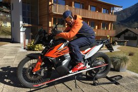 30 Jahre Jubiläums Bike Wochen Person mit Skihelm und Ski auf Motorrad vor Holzhäusern im Gebirge