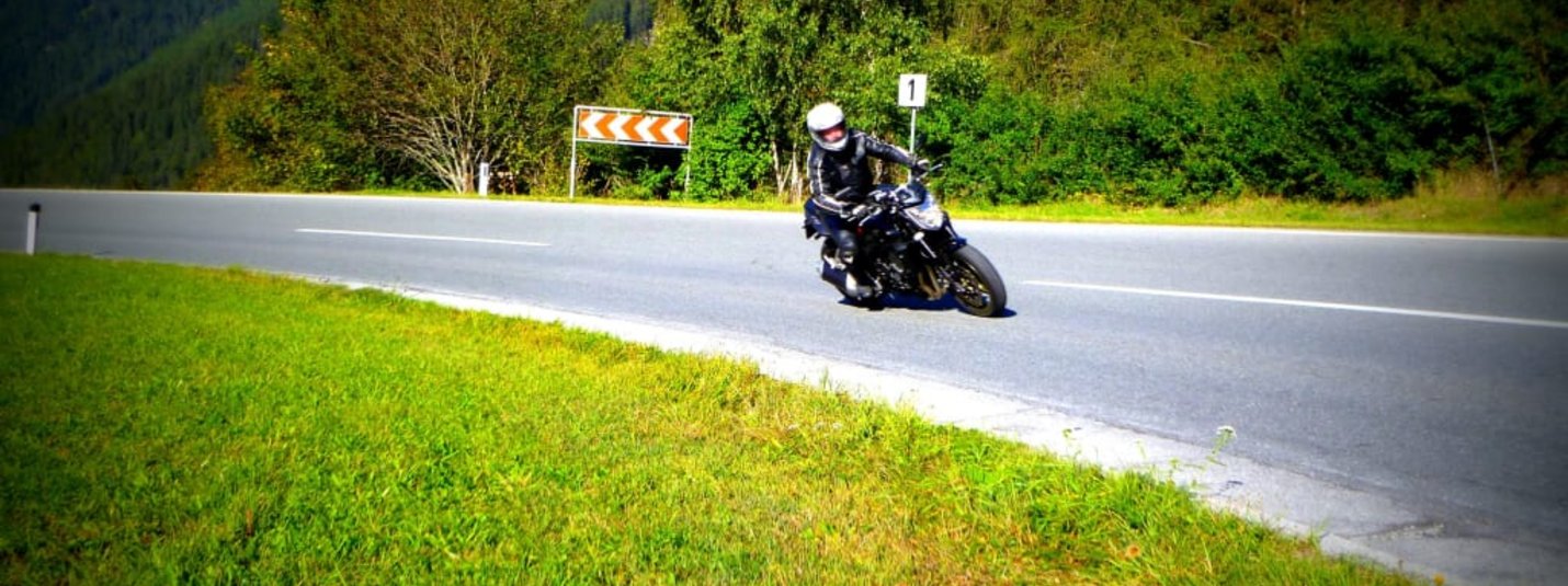 Motorradpauschale Motorradfahrer in Kurve auf Landstraße mit Bergen und Bäumen im Hintergrund
