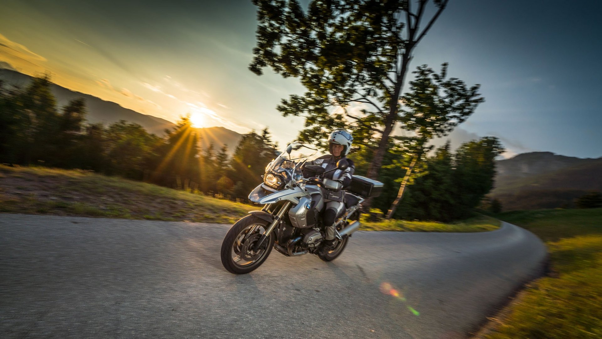Motorradfahrer auf kurviger Straße bei Sonnenuntergang in ländlicher Umgebung