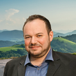 Mann in Sakko vor grünen Hügeln und bewölktem Himmel