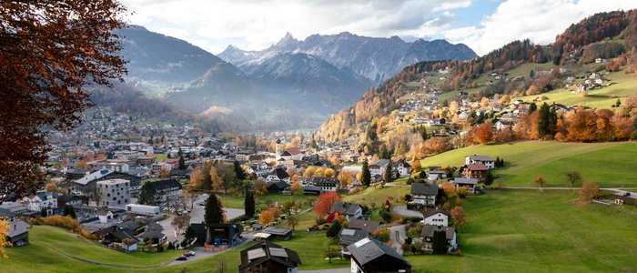 Bergdorf mit Häusern und grünen Wiesen im Herbst vor bewölkten Alpen