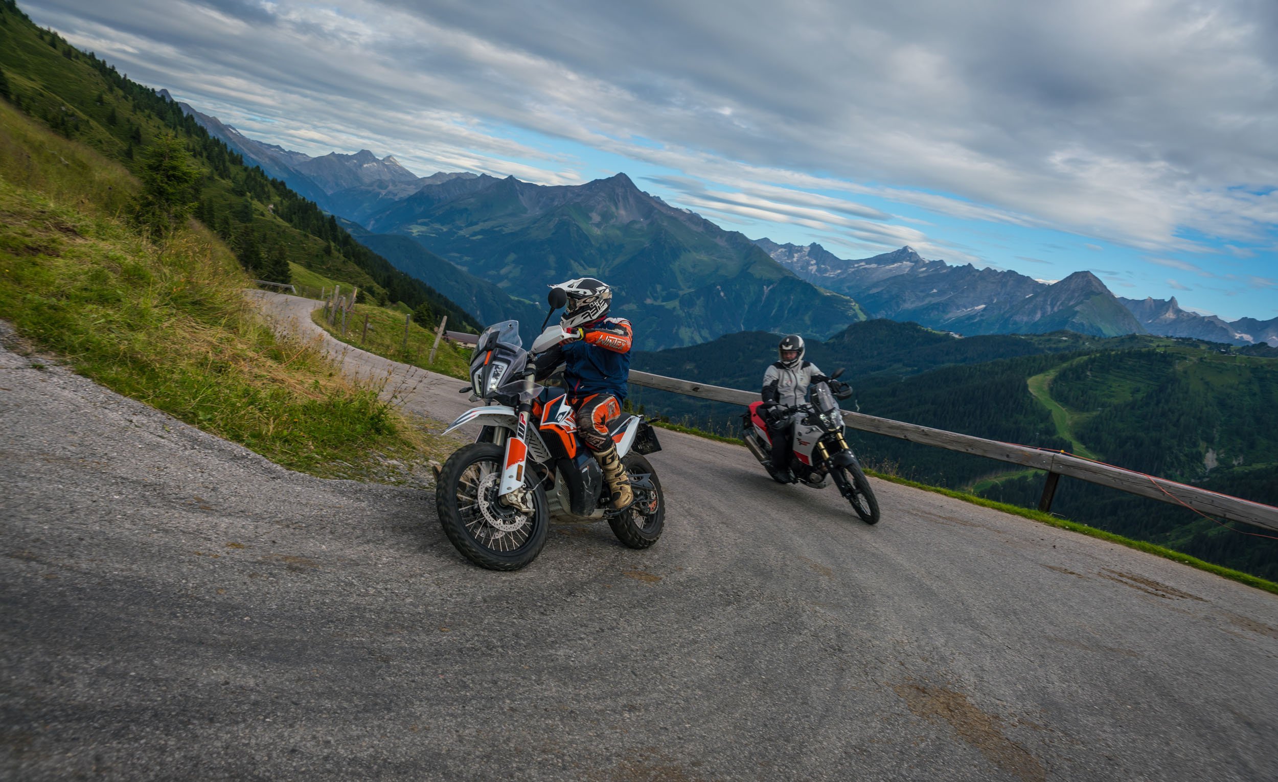 Motorradfahrer auf kurviger Bergstraße mit Alpen im Hintergrund