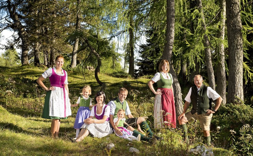 Familie in traditioneller Tracht sitzt und steht im Wald an einem sonnigen Tag