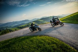 Biker Week Zwei Motorradfahrer auf kurviger Bergstraße mit grünen Hügeln im Hintergrund