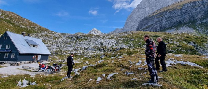 Ferienregion Wolfsberg – Region Lavanttal © Viktor Sator Drei Männer in Motorradkleidung wandern in bergiger Landschaft bei Hütte