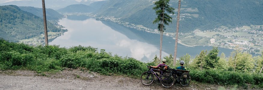 Gravel-Wundertüte Wörthersee © Region Wörthersee Rosental Tourismus GmbH - Chris Perkles Zwei Radfahrer sitzen auf einem Bergweg mit Blick auf einen See und Berge.