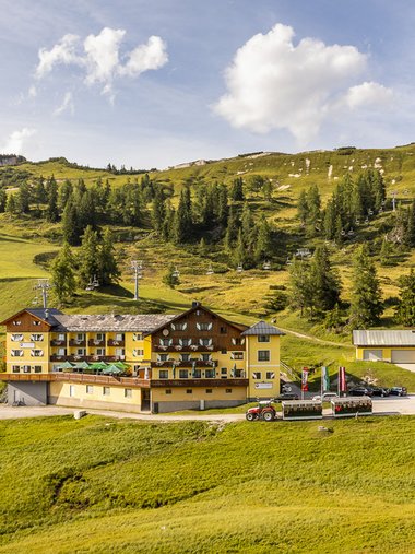 Hotel in grüner Berglandschaft mit Sessellift und Traktor im Vordergrund