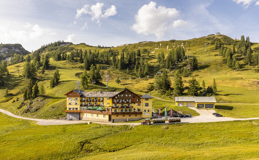 Hotel in grüner Berglandschaft mit Sessellift und Traktor im Vordergrund