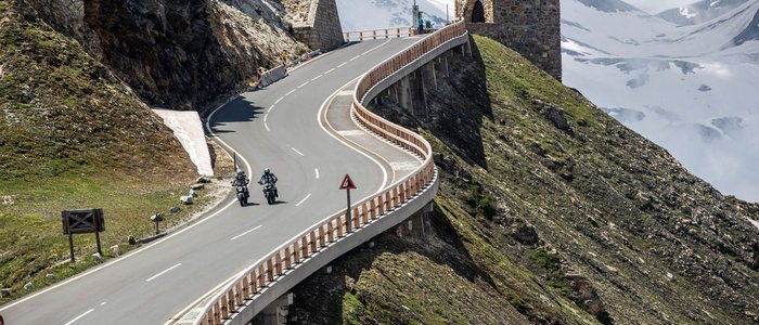 Großglockner – Hohe Tauern © Arturo Rivas Kurvige Bergstraße mit Motorradfahrern und historischen Grenzsteinen bei Schnee