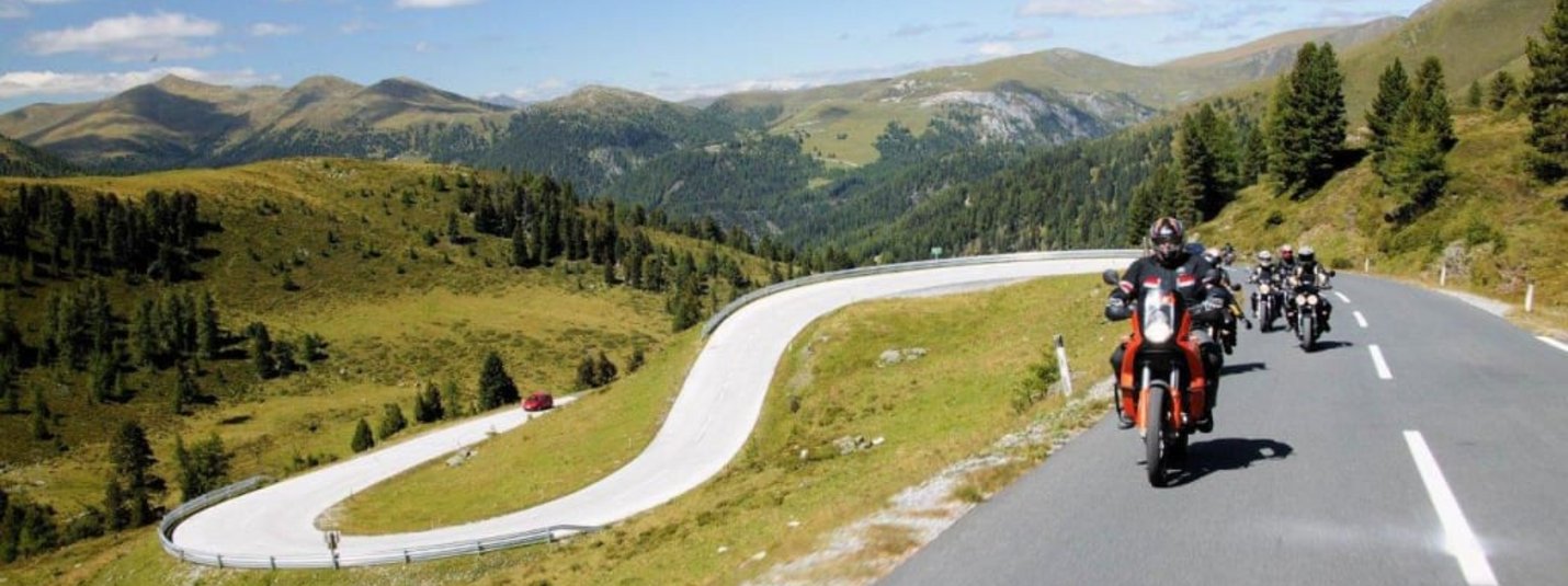 Touren- und Wanderwoche für Motorradfahrer Motorradfahrer fahren auf kurviger Bergstraße unter blauem Himmel