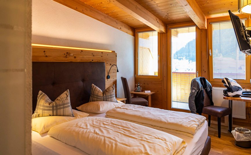 Gemütliches Schlafzimmer mit zwei Betten, Holzwänden und Balkon mit Bergblick