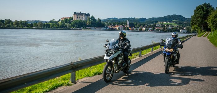 Motorradurlaub in Oberösterreich © Moppetfoto.de Zwei Motorradfahrer fahren neben einem Fluss mit einer Burg im Hintergrund