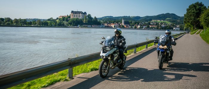 Mühlviertel © Moppetfoto.de Zwei Motorradfahrer fahren neben einem Fluss mit einer Burg im Hintergrund