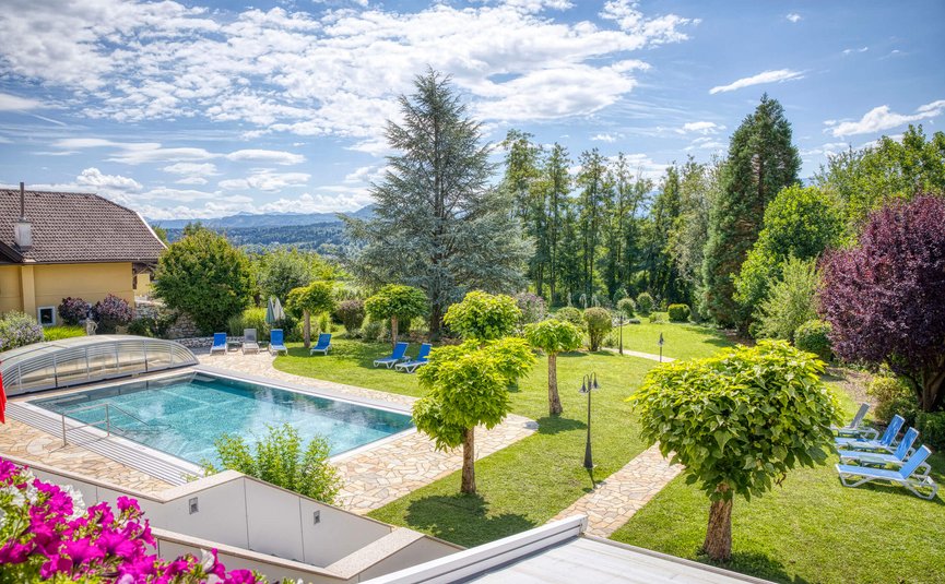Hotel Marienhof – mein Refugium **** © Bianca Wagner Schwimmbad mit Liegestühlen und gepflegtem Garten mit Bäumen und Bergen im Hintergrund.