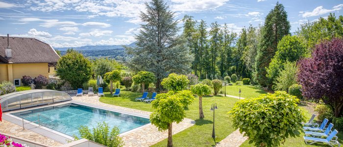 Hotel Marienhof – mein Refugium **** © Bianca Wagner Schwimmbad mit Liegestühlen und gepflegtem Garten mit Bäumen und Bergen im Hintergrund.