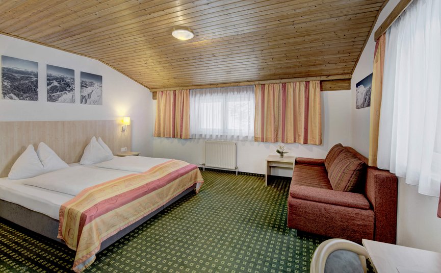 Gemütliches Hotelzimmer mit Doppelbett, Sofa und Holzdach