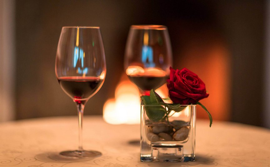 Zwei Weingläser und eine rote Rose in einem Glas vor einem Kamin