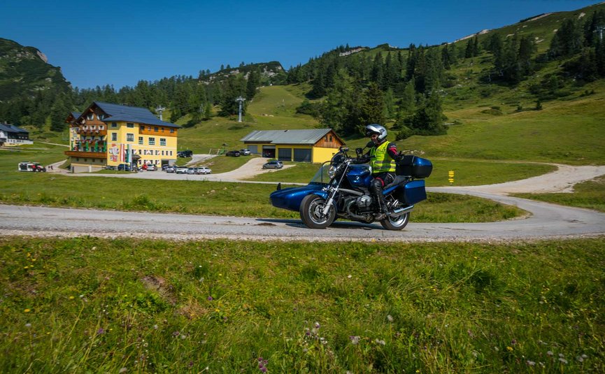 Motorradfahrer mit Seitenwagen auf Landstraße vor Alpenhotel bei sonnigem Wetter