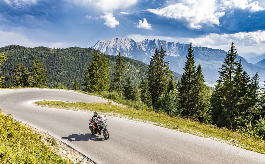 Motorradfahrer auf kurviger Bergstraße mit Tannen und Bergen im Hintergrund