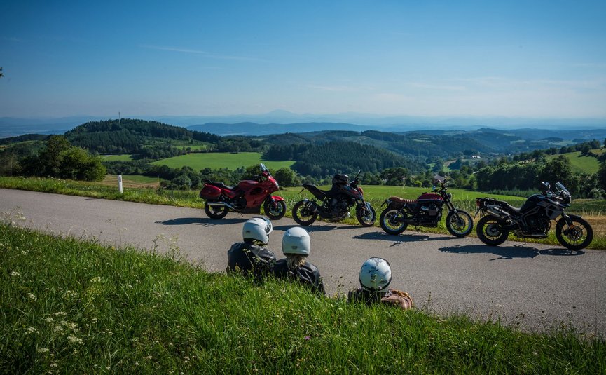 Motorradurlaub in Niederösterreich © Moppetfoto.de Drei Motorradfahrer sitzen am Straßenrand mit Blick auf grüne Hügel und blaue Berge