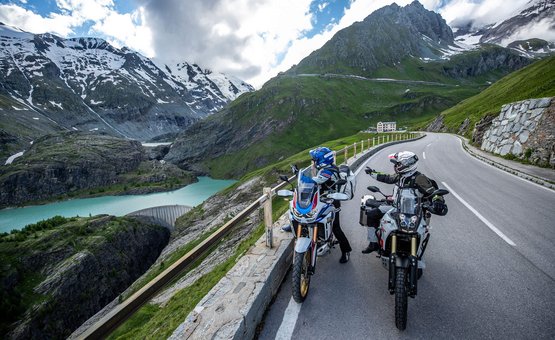 Motorradurlaub im SalzburgerLand © Arturo Rivas Zwei Motorradfahrer auf Alpenstraße mit Bergsee und schneebedeckten Gipfeln