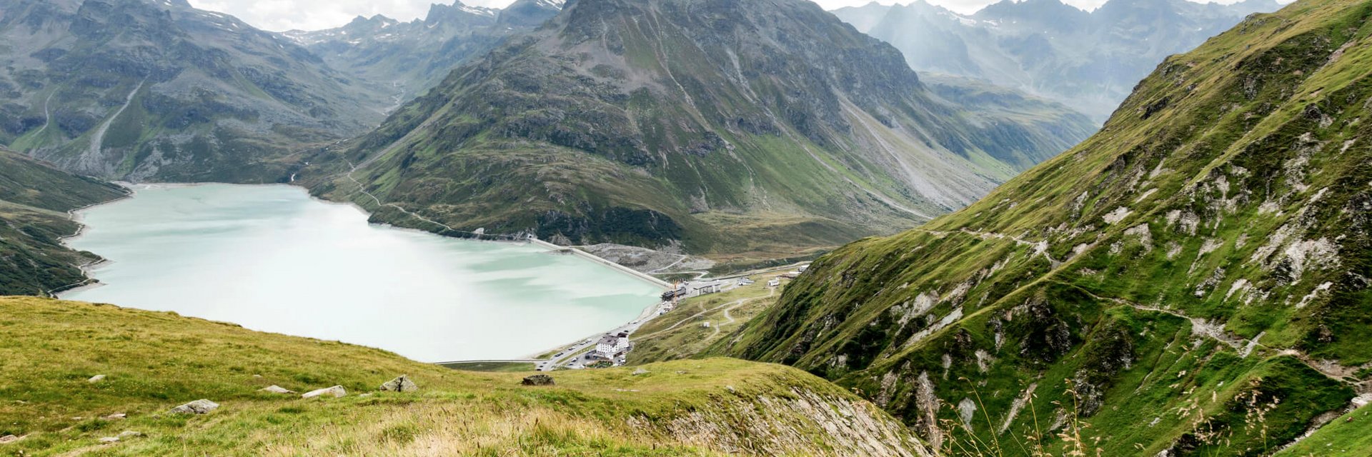 Bergsee und grüne Alpenhänge bei bewölktem Himmel