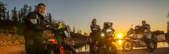 Motorradurlaub: Großglockner – Hohe Tauern © Moppetfoto.de Drei Motorradfahrer stehen am Seeufer bei Sonnenuntergang