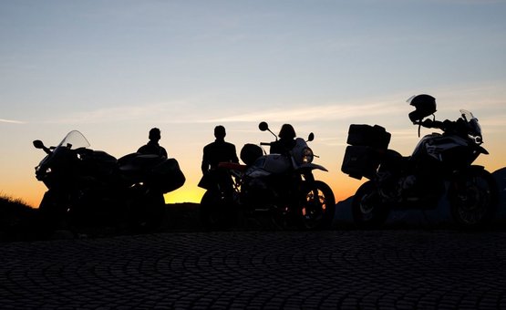 Auf die Berge - fertig - los ! ab € 398,- pro Person Drei Motorradfahrer mit ihren Motorrädern bei Sonnenuntergang