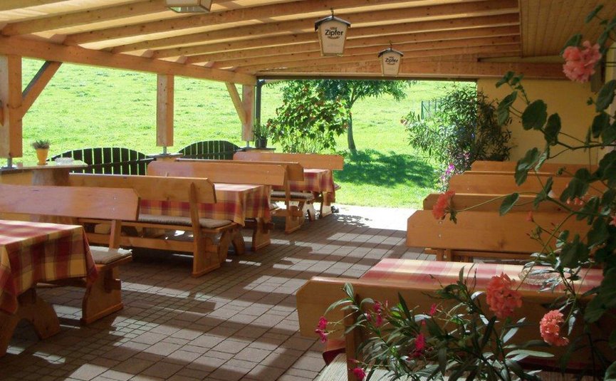 Gast-Hof-Laden Schneeweiss *** © Gast-Hof-Laden Schneeweiss Überdachte Terrasse mit Holztischen, Bänken und Blumen vor grüner Wiese
