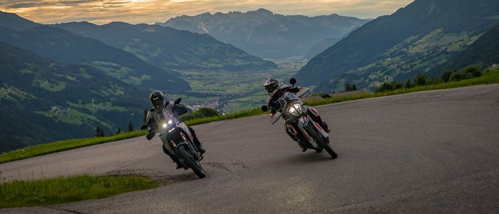 Zwei Motorradfahrer in den Alpen fahren bei Sonnenuntergang auf kurviger Bergstraße