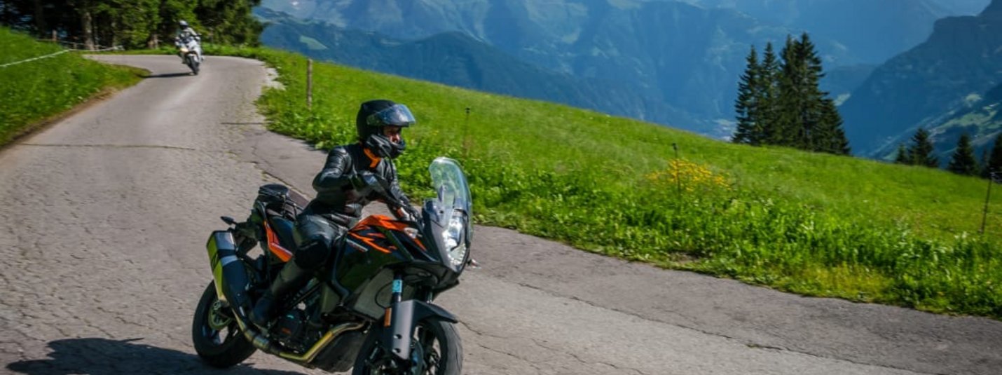 Motorradfahrer fährt auf bergiger Straße mit Blick auf Alpen