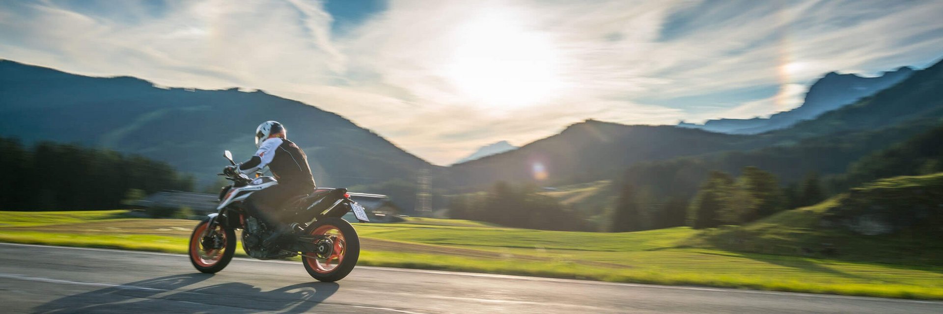 Motorradfahrer fährt auf Bergstraße bei Sonnenuntergang