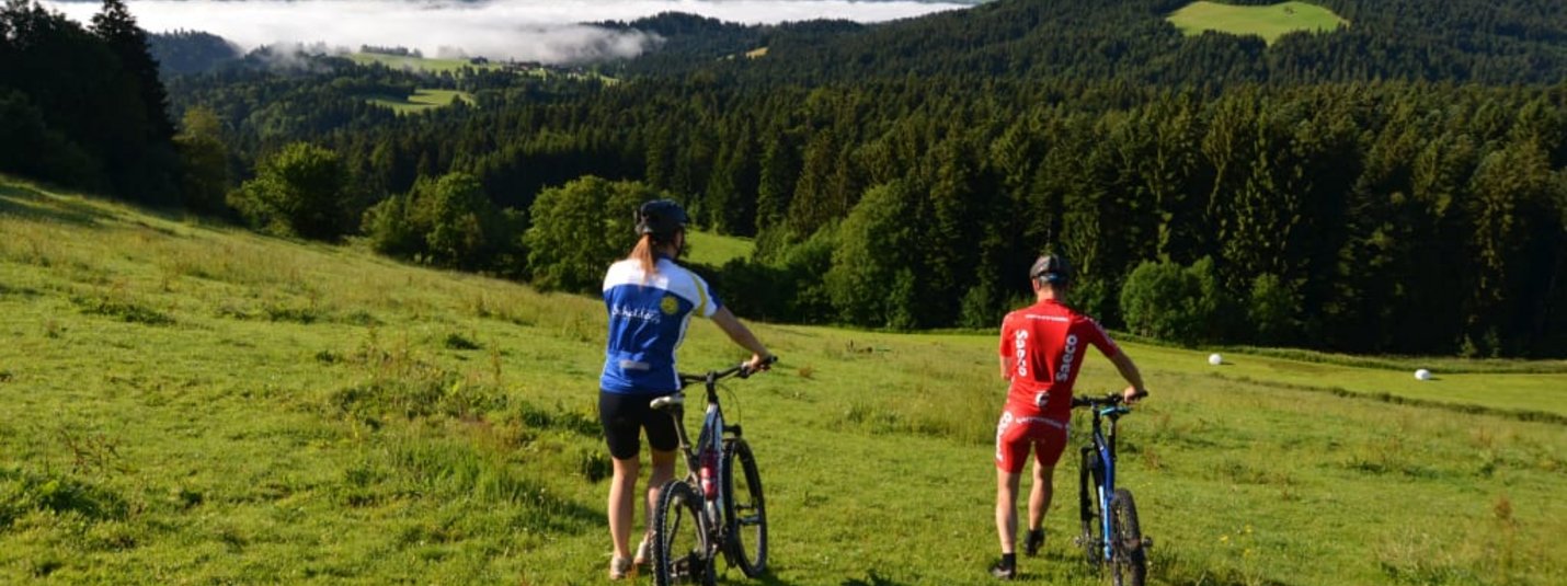 Das Allgäu  per Bike erkunden Zwei Radfahrer schieben ihre Fahrräder auf einer Wiese mit Bergen im Hintergrund
