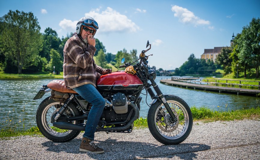 Mann mit Helm auf Motorrad an Flussufer bei sonnigem Wetter