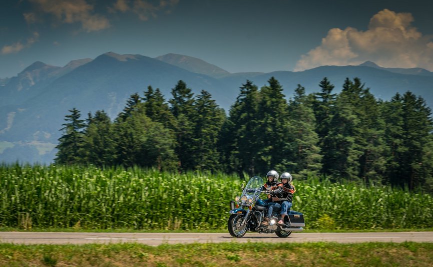 Motorradurlaub in der Region 3 Zinnen – Kronplatz – Eisacktal © Moppetfoto.de Zwei Motorradfahrer fahren auf Landstraße vor Wald und Bergen