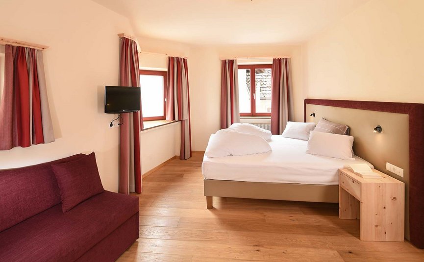 Hotel & Südtiroler Gasthaus Der Gassenwirt *** © Hotel Gassenwirt Helles Schlafzimmer mit Doppelbett, Fernseher und rotem Sofa