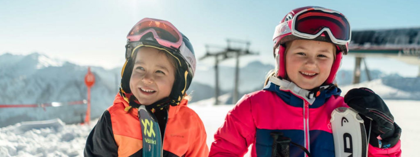 Leistbarer Familienskiurlaub Zwei lächelnde Kinder in Skiausrüstung im Schnee am sonnigen Berg