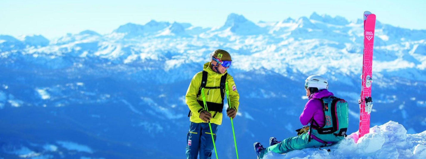 Zwei Skifahrer auf schneebedecktem Berg mit Alpenpanorama