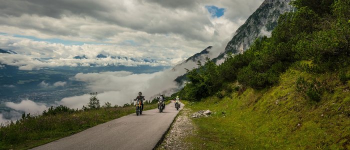 Zillertal – Gerlos Alpenstraße © Moppetfoto.de Drei Motorräder fahren auf einer Bergstraße mit Wolken und grüner Landschaft
