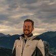 Zwei Motorradfahrer mit ihren Motorrädern vor bergiger Landschaft bei bewölktem Himmel
