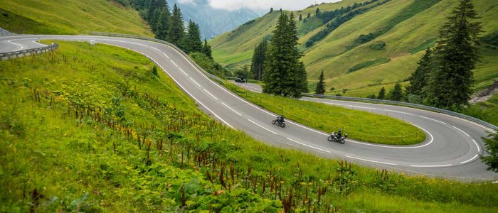 Kurvige Bergstraße mit zwei Motorradfahrern und grünen Hügeln