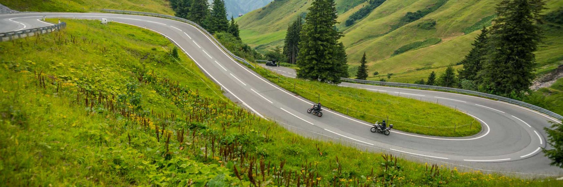 Kurvige Bergstraße mit zwei Motorradfahrern und grünen Hügeln