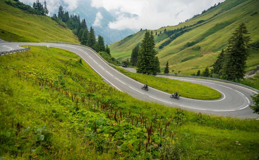 Motorradurlaub im Lechtal – Hahntennjoch © Moppetfoto.de Kurvige Bergstraße mit zwei Motorradfahrern und grünen Hügeln