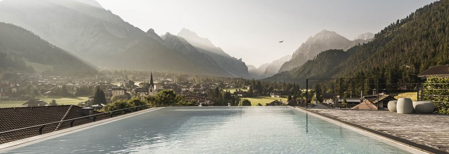 Prädikat: Außergewöhnlich © Hannes Niederkofler Infinity-Pool mit Blick auf ein Dorf und Berge im Morgenlicht