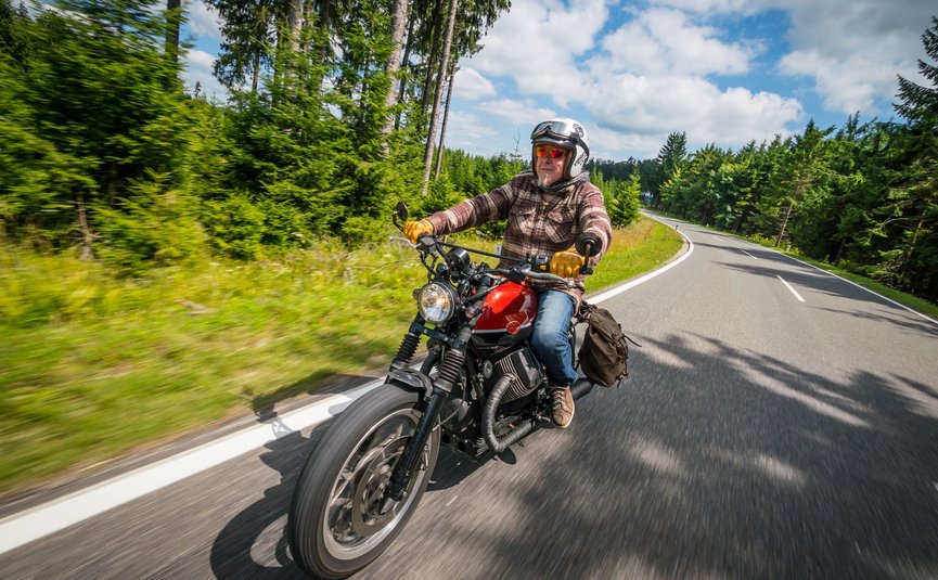 Älterer Mann fährt Motorrad auf kurviger Waldstraße bei Tageslicht