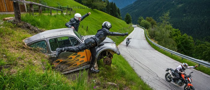 Motorradfahrer winken von einem alten Auto am Straßenrand in den Bergen