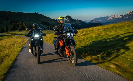 Zwei Motorradfahrer fahren auf Bergstraße mit grünen Wiesen und Bergen im Hintergrund
