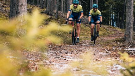 Gravel-Wochenende in San Vigilio © Jens Scheibe Zwei Radfahrer fahren auf einem Waldweg zwischen Bäumen